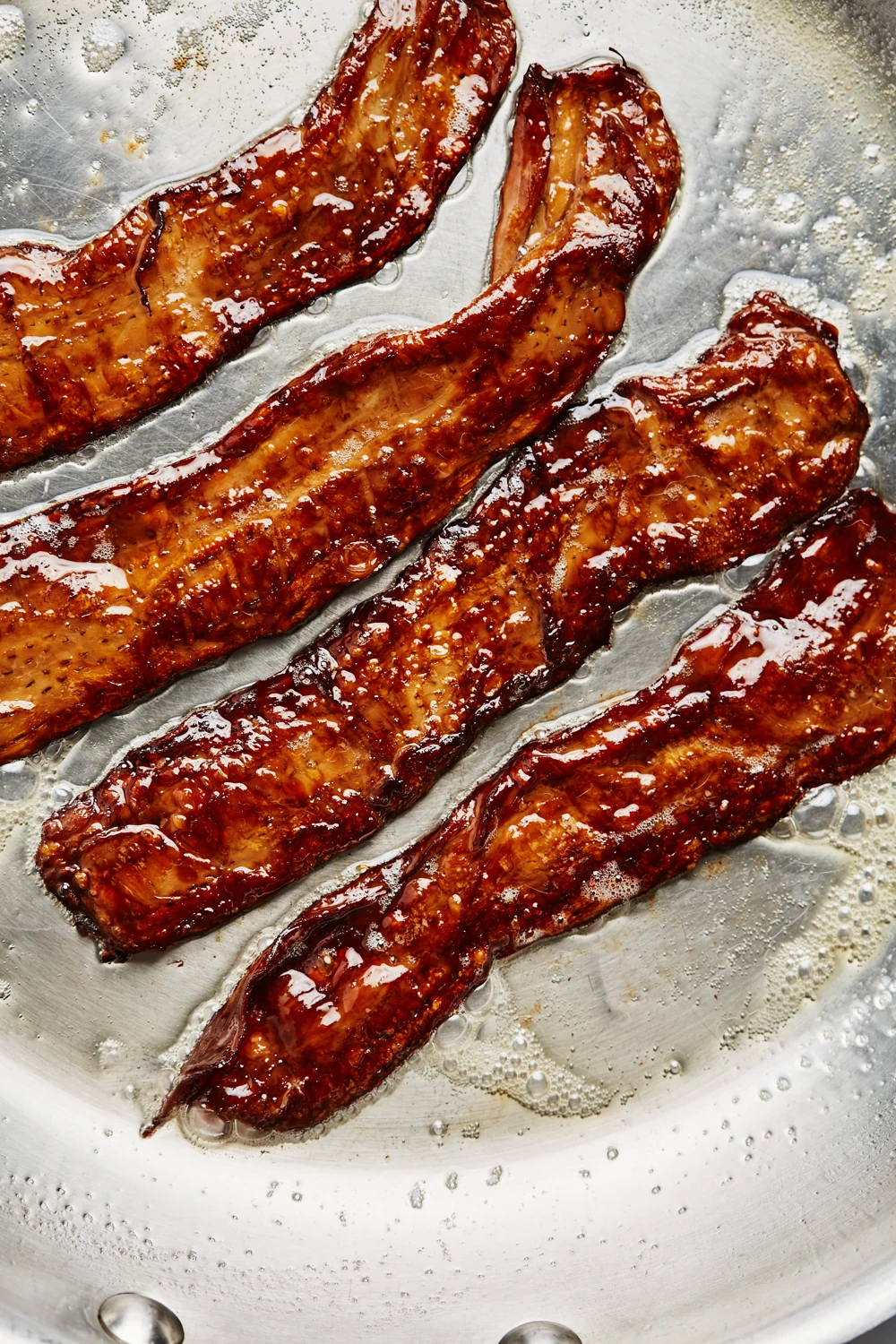 Four MyBacon strips browning in a stainless steel pan
